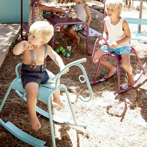 Dos niños jugando con sus caballitos Adada de Fermob en algun jardin o patio al exterior