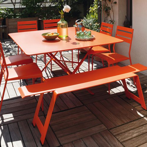 Mesa Cargo naranja zanahoria cuadrada con sillas y una banca en una terraza al exterior