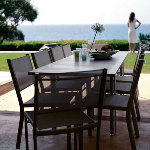 Comedor Costa de diseño Fermob en una terraza en un lago al exterior y con un jardin de fondo