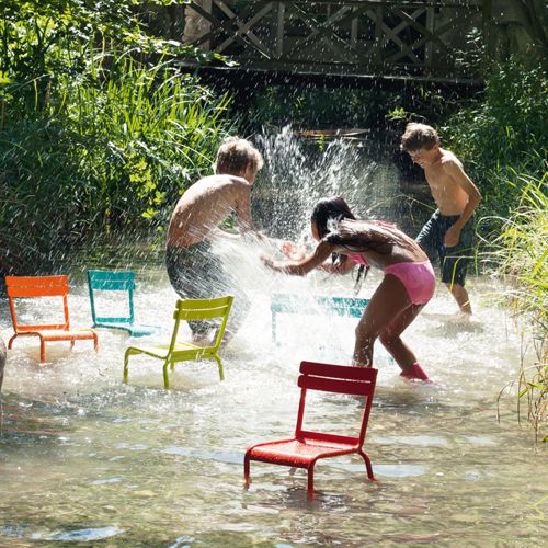 Niños jugando en un rio con sillas Luxembourg Kids de aluminio fabricadas por Fermob